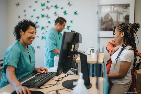 Happy female receptionist talking with mother carrying daughter at receptionist desk in hospital